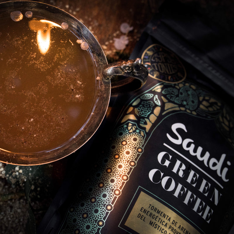 Se puede observar una taza servida con Saudi  Green Coffee reflejando la luz de una vela junto a una bolsa del producto.